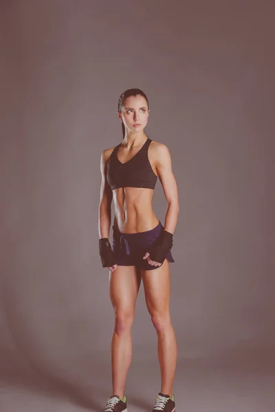 Muskulös ung kvinna poserar i sportkläder mot svart bakgrund. — Stockfoto
