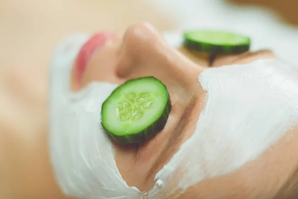 Beautiful young woman receiving facial mask of cucumber in beauty salon — Stock Photo, Image