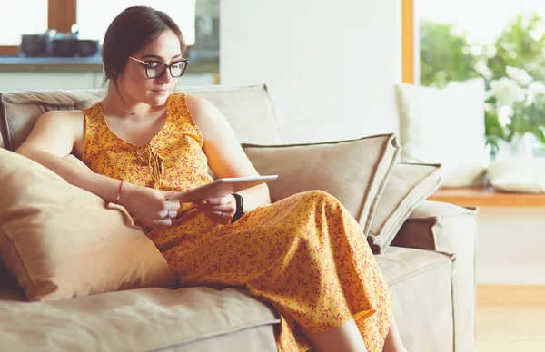 Vakker ung kvinne som bruker nettbrett på sofaen hjemme i stua – stockfoto