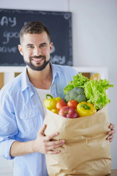 Man som håller papperspåse full av matvaror på köksbakgrund. Shopping och hälsosam mat koncept — Stockfoto