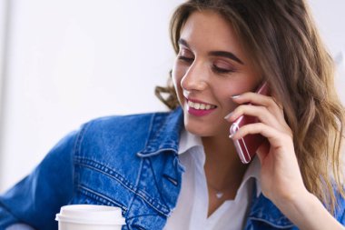 Kafede kahve içip cep telefonuyla konuşan genç bir kadın.