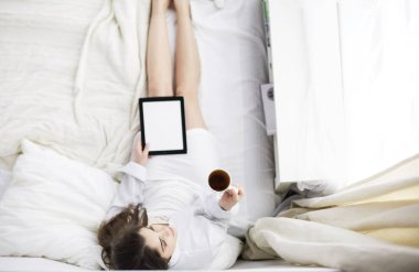Sabahları yatakta otururken tablet kullanan ve kahve içen kadın portresi