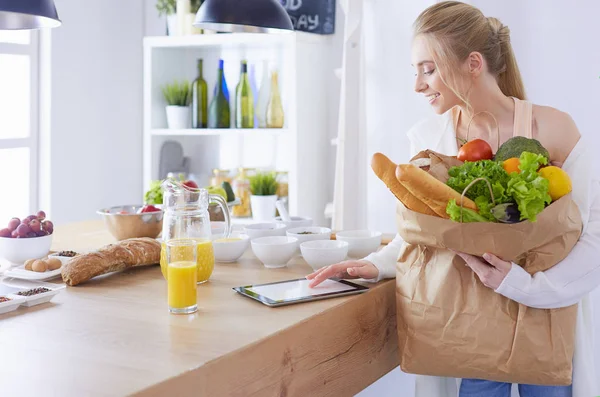 Giovane donna che tiene borsa della spesa con verdure. In piedi in cucina — Foto Stock