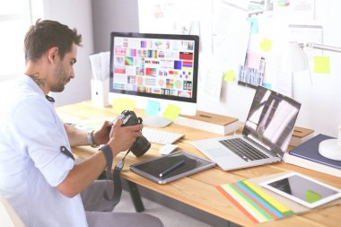 İnternette çalışırken bilgisayarın ve dizüstü bilgisayarın önünde grafik stüdyosunda oturan genç tasarımcının portresi.