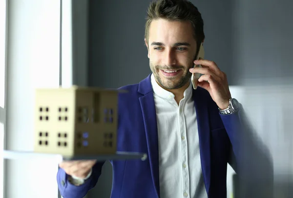 Homme d'affaires tenant maison miniature à portée de main debout dans le bureau . — Photo