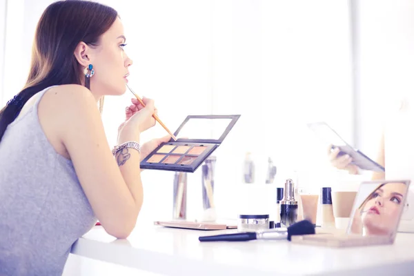 Mujer morena aplicando maquillaje para una cita nocturna frente a un espejo — Foto de Stock