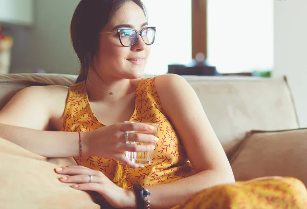 Tyttö juo vettä istuu sohvalla kotona — kuvapankkivalokuva
