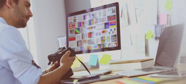 İnternette çalışırken bilgisayarın ve dizüstü bilgisayarın önünde grafik stüdyosunda oturan genç tasarımcının portresi.