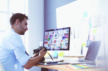 İnternette çalışırken bilgisayarın ve dizüstü bilgisayarın önünde grafik stüdyosunda oturan genç tasarımcının portresi.