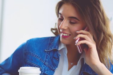 Kafede kahve içip cep telefonuyla konuşan genç bir kadın.