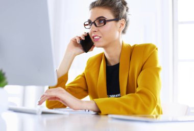 İş kadını ofiste bilgisayar ve cep telefonu kullanarak işine konsantre oluyor.