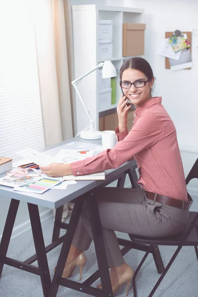 Porträt einer attraktiven Modedesignerin, die lächelnd am Schreibtisch sitzt — Stockfoto