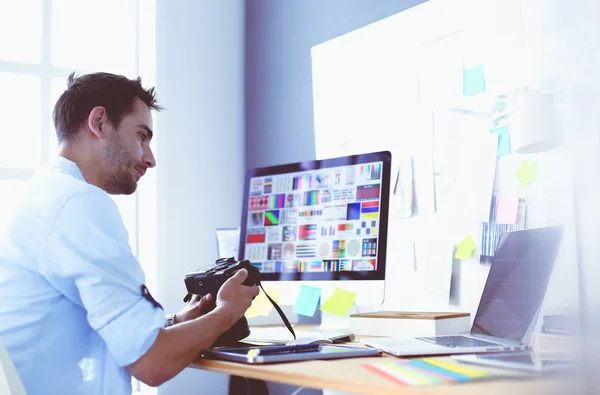 Retrato del joven diseñador sentado en el estudio gráfico frente a la computadora portátil y el ordenador mientras trabaja en línea. — Foto de Stock