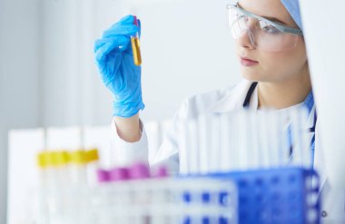 Bir kadın tıbbi veya bilimsel araştırmacı ya da kadın doktor laboratuarda bir test tüpü dolusu temiz çözeltiye bakıyor.
