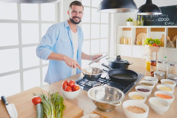 Homme suivant la recette sur tablette numérique et la cuisine savoureuse et saine dans la cuisine à la maison — Photo