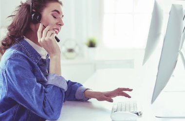 Ofiste kulaklık takıp laptopla çalışan mutlu, genç bir kadın.