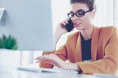 İş kadını ofiste bilgisayar ve cep telefonu kullanarak işine konsantre oluyor.