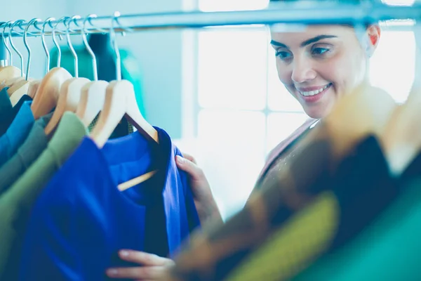 Beautiful young stylist near rack with hangers