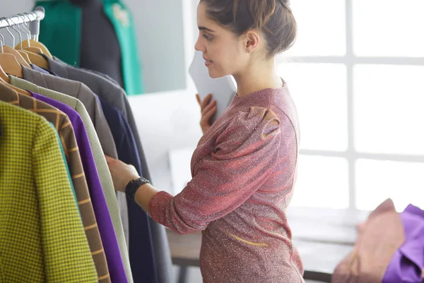 Schöne junge Stylistin in der Nähe von Gestell mit Kleiderbügeln — Stockfoto