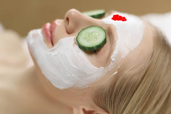 Beautiful young woman receiving facial mask of cucumber in beauty salon — Stock Photo, Image