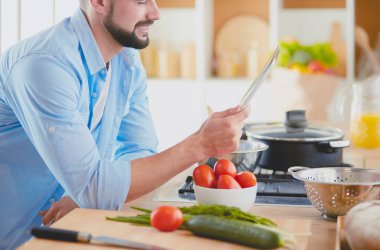 Dijital tablet ve yemek pişirme tarifine uyan bir adam evdeki mutfakta lezzetli ve sağlıklı yemekler pişiriyor.