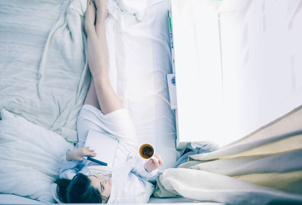 Портрет женщины с помощью планшета и пить кофе, сидя на кровати утром