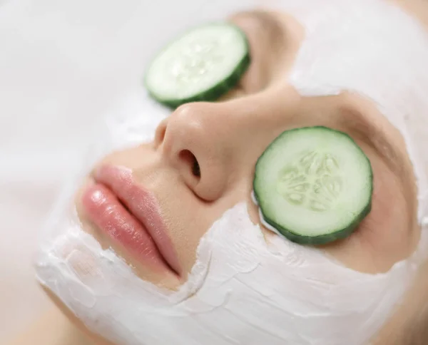 Vacker ung kvinna som får ansiktsmask av gurka i skönhetssalong — Stockfoto