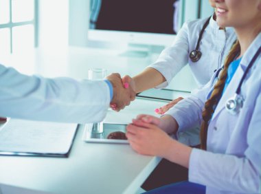 Doktor beyaz arka planda izole edilmiş bir hastayla el sıkışıyor.