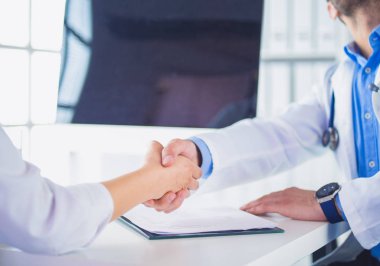 Doktor masadaki hastaya el sıkışıyor.