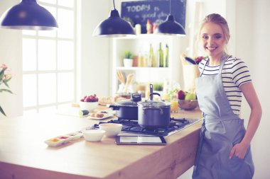 Mutfakta yemek yapmak için tablet bilgisayar kullanan genç bir kadın.