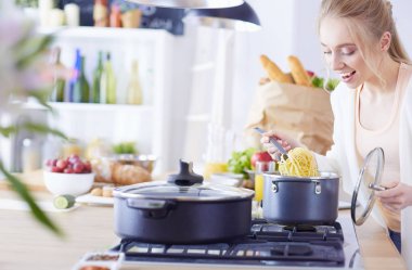 Evdeki mutfakta yemek pişiren güzel genç bir kadın.