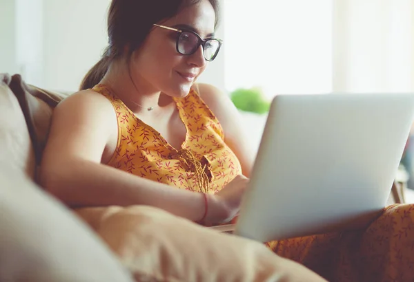 Giovane donna seduta sul divano che lavora sul computer portatile a casa — Foto Stock