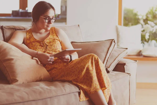 Oturma odasındaki kanepede tablet kullanan güzel genç bir kadın. — Stok fotoğraf