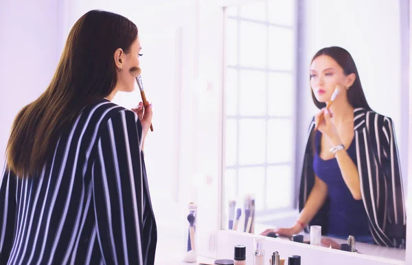 Schönes Mädchen, das in den Spiegel schaut und Kosmetik mit einem großen Pinsel anwendet — Stockfoto