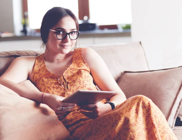 Güzel genç esmer kadın evde kanepe veya kanepe üzerinde onu tablet bilgisayar kullanarak oturan ve gülümseyen — Stok fotoğraf