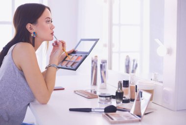 Esmer bir kadın aynanın önünde akşam randevusunu telafi etmek için başvuruyor.