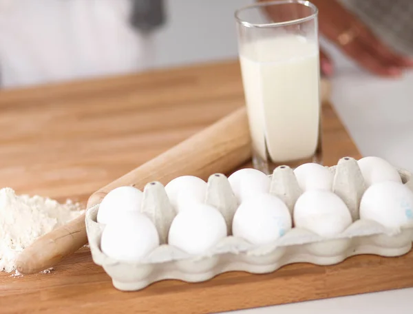 Baking background with eggs, raw eggs in a dish, eggshells, flour, rolling pin and whisk on a wooden background — Stock Photo, Image