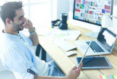 İnternette çalışırken bilgisayarın ve dizüstü bilgisayarın önünde grafik stüdyosunda oturan genç tasarımcının portresi.