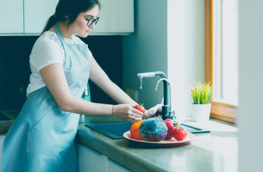 Mutfak lavabosunda domates yıkayan bir kadın.