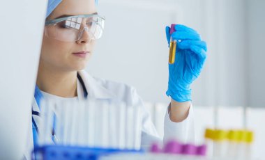 Bir kadın tıbbi veya bilimsel araştırmacı ya da kadın doktor laboratuarda bir test tüpü dolusu temiz çözeltiye bakıyor.
