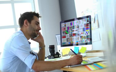 İnternette çalışırken bilgisayarın ve dizüstü bilgisayarın önünde grafik stüdyosunda oturan genç tasarımcının portresi.