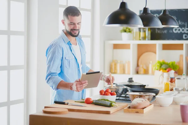 Manusia mengikuti resep pada tablet digital dan memasak makanan lezat dan sehat di dapur di rumah — Stok Foto