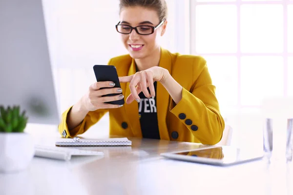 Retrato de la mujer de negocios usando el teléfono móvil y mensajes de texto mientras está sentada en el escritorio delante de la computadora portátil — Foto de Stock