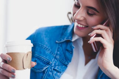 Kafede kahve içip cep telefonuyla konuşan genç bir kadın.