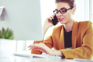 İş kadını ofiste bilgisayar ve cep telefonu kullanarak işine konsantre oluyor.