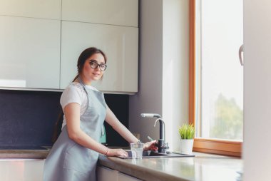 Bir bardak suyu paslanmaz çelikten, krom musluktan ya da musluktan dolduran kadın.