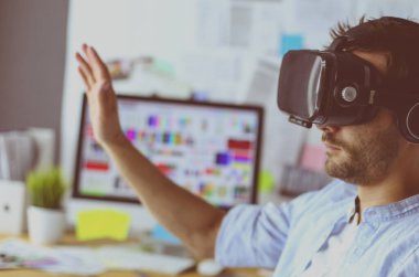 Genç erkek yazılım programcısı ofiste üç boyutlu sanal gerçeklik gözlükleriyle yeni bir uygulama test ediyor..
