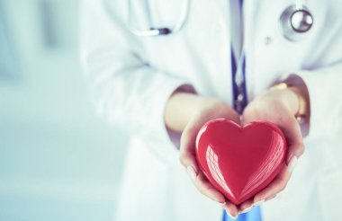 Female doctor with stethoscope holding heart, on light background clipart