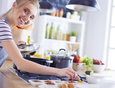 Evdeki mutfakta yemek pişiren güzel genç bir kadın.