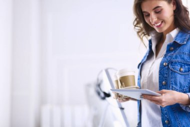 Gülümseyen kadın kahve içiyor ve kafede tablet kullanıyor.